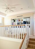 Cosy library on gallery with fitted shelving, wooden balustrade and ceiling fan