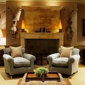 Comfortable reading chairs in front of open fireplace and vase-like ornaments on wall next to lamps on mantelpiece in traditional living room