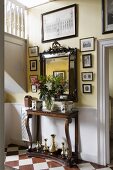 Bouquet of lilies on antique console table, mirror and old photos and drawings in entrance hall of English country house