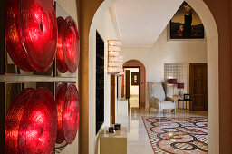 Wall lamp made of red discs in anteroom with view through arched doorway into elegant foyer with patterned tiled floor
