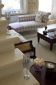 Seating area in living room with elegant, dark wood country house furniture with checked upholstery; candles on stone steps in foreground