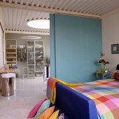 Colourful checked bed linen in bedroom and view through light blue sliding door into ensuite bathroom