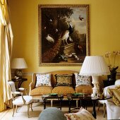 Table lamp with white fabric lampshade on small side table in front of Rococo bench and old painting on yellow-painted wall