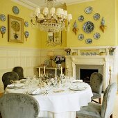 Festively set dinner table in front of open fireplace and decorative plates on yellow-painted walls