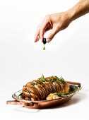 A hand squeezing olive oil out of an olive onto a veal roulade