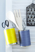 Decorated tin cans being used as storage tins for kitchen utensils hanging on a wall