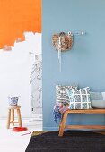 Cushions on bench in front of light blue painted wall and stool in front of wall partially painted orange