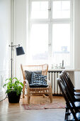 Cushions on wicker chair next to standard lamp below window in corner of living room with traditional ambiance