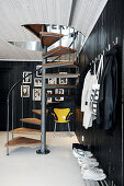 Cloakroom foyer with black-painted wooden walls and spiral staircase: black and white portraits and bright yellow classic chair in background