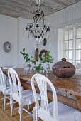White chairs at rustic wooden table below chandelier with glass droplets in simple dining room