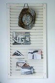 Cowboy hat and brochures hung on white, louvred shutter used as magazine rack mounted on wall