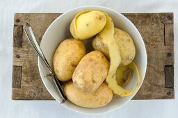 Potatoes and a peeler in a bowl