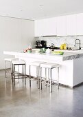 Open-plan, white designer kitchen with bar stools at breakfast bar