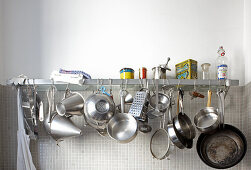 Various stainless steel pots and pans hanging from wall-mounted shelf
