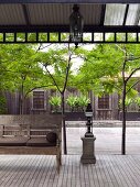 Asian bench under a covered wooden terrace with a view of an inviting green courtyard