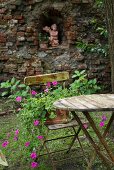 Old garden table and terracotta planter on chair; angel statue in niche of brick wall in background