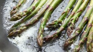 Green asparagus being fried in a pan of butter