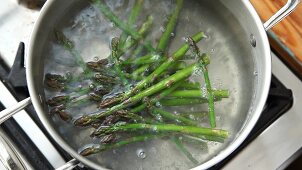 Green asparagus being added to a pot of boiling water
