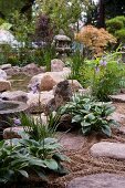Large stones and plants on edge of garden pond with Japanese lamp and Japanese maple in background