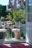 View through open balcony door of white bistro furniture with pale pink cloth on coffee table and flowering oleander in background