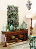 Sammlung verschiedener Vasen und Teller aus Ton auf einem antiken Sideboard mit Fransenbordüre unter einem abstrakten Glasgemälde