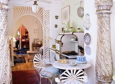 Decorated columns and a semi-transparent arched hallway separating the kitchen with a vintage wood stove and eye catching iron chairs in the living area