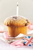 A cupcake decorated with a candle with Union Jack decorations next to it