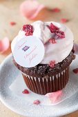 A chocolate cupcake topped with cream, candied rose petals and a Union Jack decoration