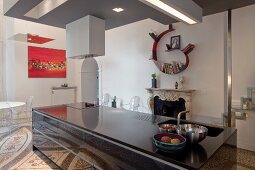 Monolithic, black kitchen island in front of open fireplace in open-plan interior with terrazzo floor