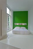 Modern bed with white bedspread against green wall on white epoxy resin floor