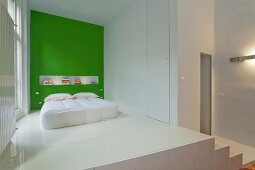 Bedroom area on platform with white epoxy resin floor and bed against green wall