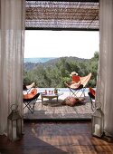 Laternen-Windlichter als Wächter der Terrassentür; Weitblick von der Terrasse mit einladenden Fledermaussesseln und Drinks auf Tabletttisch