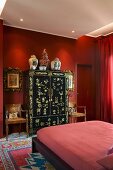 Red bedroom - modern double bed in front of Oriental-style black and gilt wardrobe against red wall