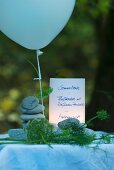 Menu card for summer party on river bank; names written on stacked pebbles, balloon and fennel fronds as table decoration