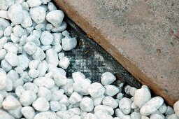 Gravel on black plastic matting next to solid stone flag