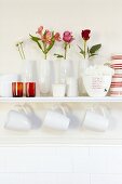 Vases of flowers on white wall-mounted shelf and mugs hanging from hooks