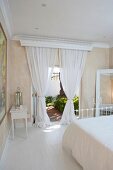 Romantisches Schlafzimmer in mediterraner Villa - weiße, luftige Vorhänge an geöffneten Terrassentüren