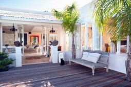 Wooden bench between palm trees on modern deck in front of Mediterranean house with open terrace doors