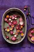 Rosarote Gartenstrohblumen, schwimmend in einer alten Zinkschale auf violetter Leinenserviette