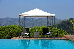 Stühle und Tisch unter der Pergola am Infinity-Pool mit Blick auf Berglandschaft