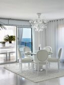 Elegant white leather chairs at round dining table in modern dining room with glass wall and sea view