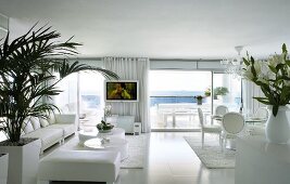 White, modern interior with white lounge and dining furniture in contemporary building with terrace and sea view