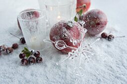 Granatäpfel, Äpfel und Beeren neben brennenden Kerzen auf Unterlage mit besprühtem Kunstschnee