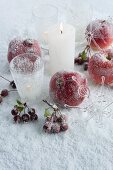 Granatäpfel, Äpfel und Beeren neben brennenden Kerzen auf Unterlage mit besprühtem Kunstschnee