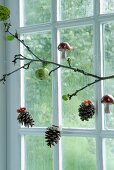Branch in front of window decorated with pine cones and fly agaric ornaments