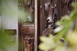 Holzgeschnitzte Eingangstür und moderne Türklingel in Hauswand