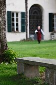 Stone bench in garden and man in front of country house villa with large entrance gate