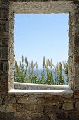 Blick durch Fensteröffnung in Natursteinmauer auf das Meer