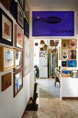Anteroom with crowded gallery of pictures and violet poster with lettering above doorway leading to improvised kitchen