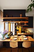 Gedeckter Esstisch in offener Küche mit Regalen an abgehängten, schwarz getönten Decken-Einbauten